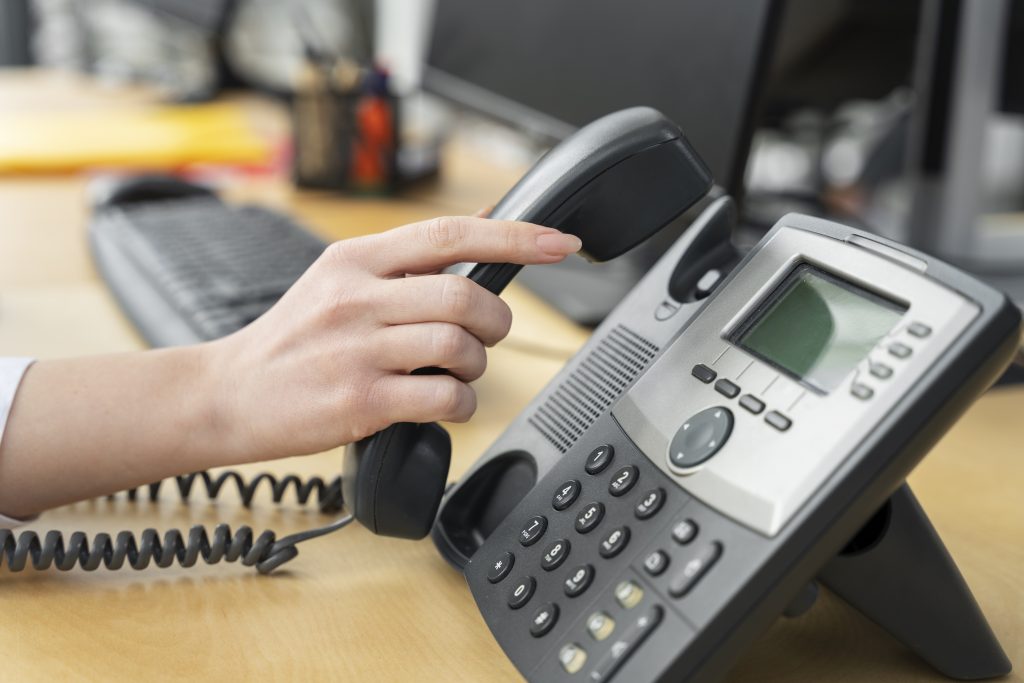 Zbliżenie na rękę sięgającą po słuchawkę telefonu biurowego na stanowisku obsługi klienta